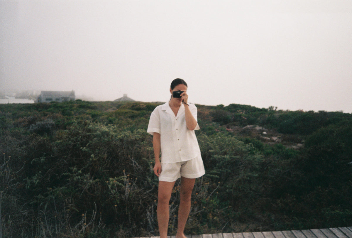 Relaxed fit short-sleeve button-up shirt and matching shorts in natural light fabric, worn barefoot on a wooden boardwalk