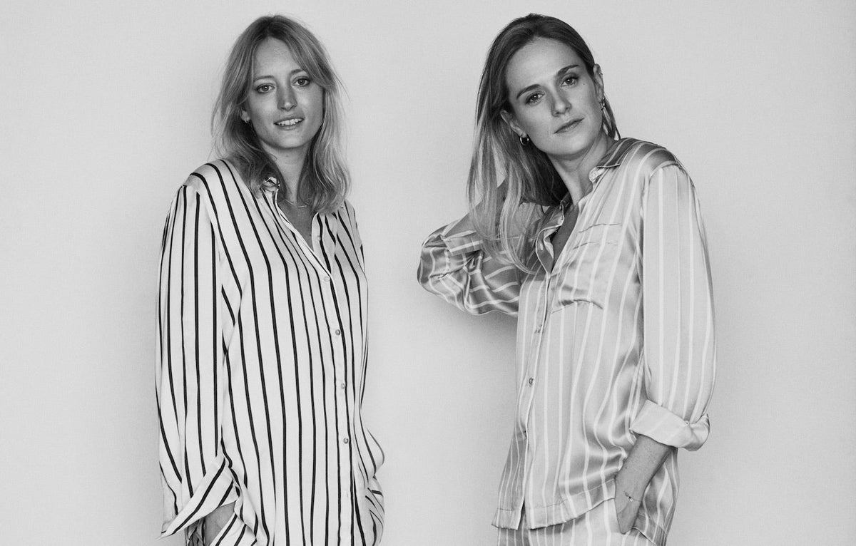 Two women in monochrome striped button-up shirts, one in loose cotton fabric, the other in satin with matching trousers