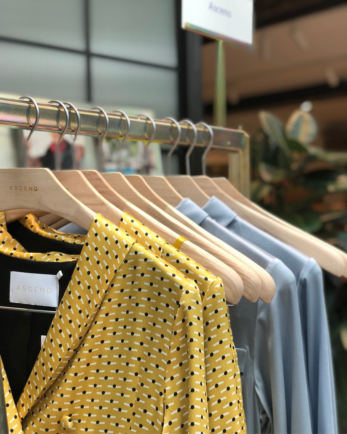 Yellow patterned silk jacket with black and white dots and light blue silk shirts hanging on wooden hangers