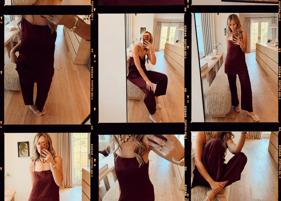 Woman modelling burgundy silk sleeveless top and wide-leg trousers in warm, softly lit room with wooden floor