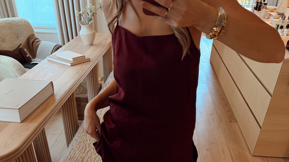 Sleeveless dark maroon dress with thin straps worn in mirror selfie from shoulders to hips in softly lit room with wooden furniture