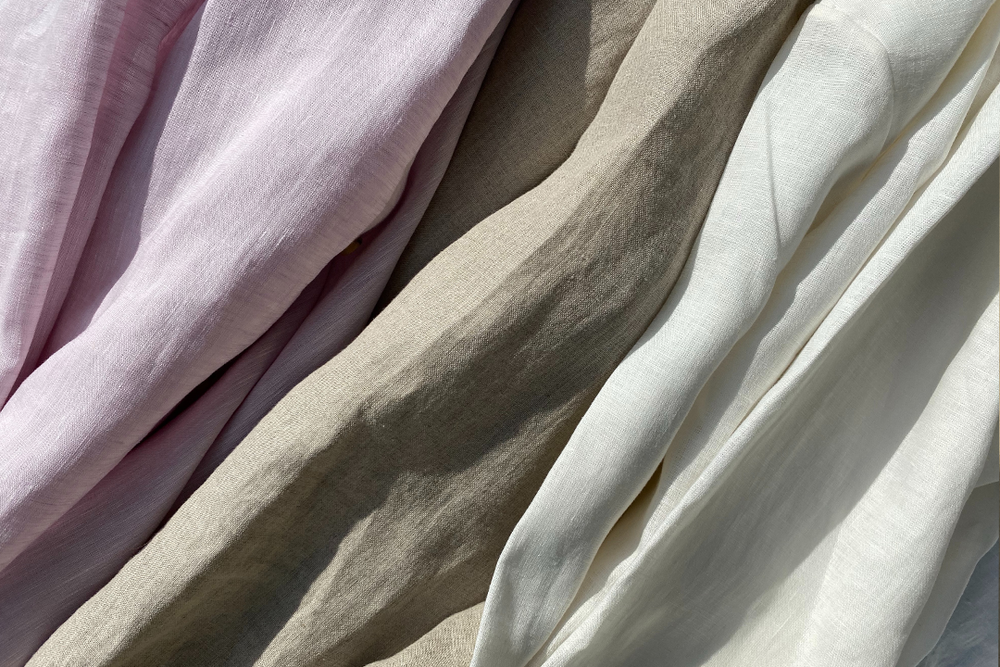 Close-up of soft pastel pink, beige, and off-white natural fabrics with visible textured weave and gentle folds