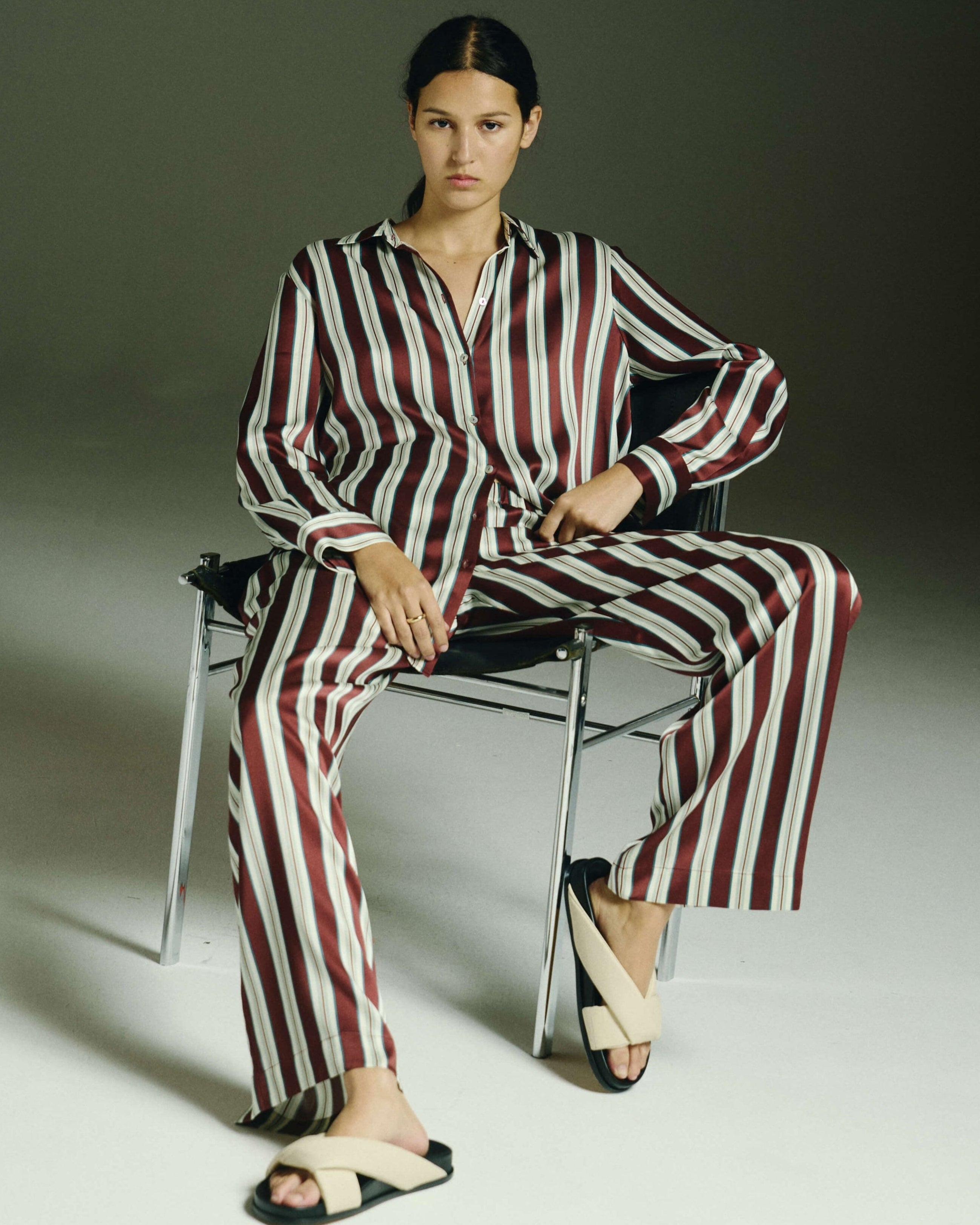 Person wearing a red and white striped outfit sitting on a chair against a gray background