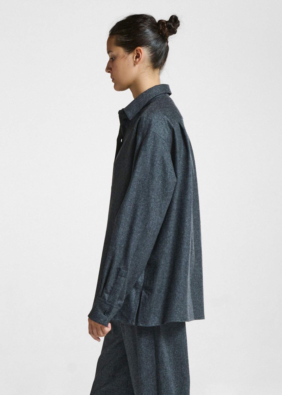 Side view of a young woman wearing a loose dark grey textured shirt and matching trousers in soft natural fabric