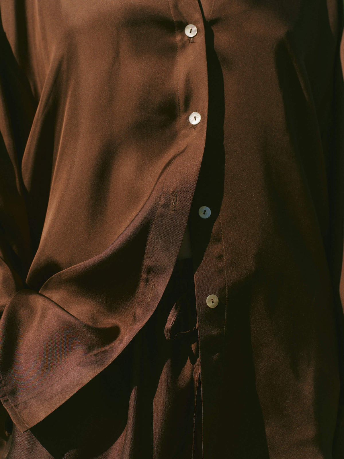 Close-up of soft dark brown silk shirt midsection with white buttons, showcasing fabric sheen and gentle folds