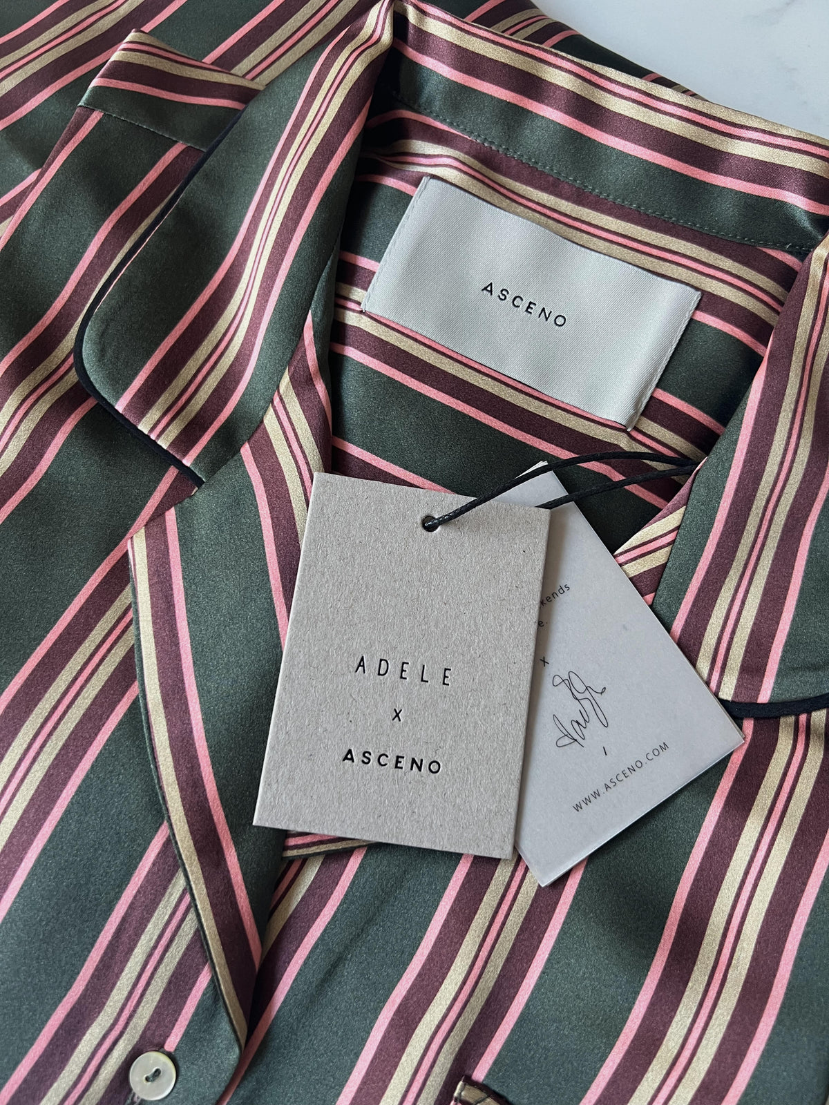 Folded Asceno silk shirt with green, pink, gold, and burgundy vertical stripes, showing label and two paper tags
