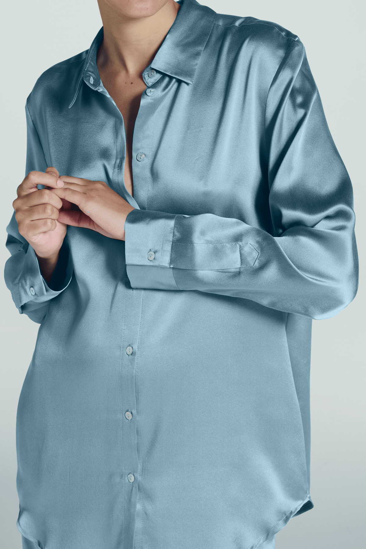 Close-up of a light blue silk shirt with long sleeves and collars, showing hands buttoning the front