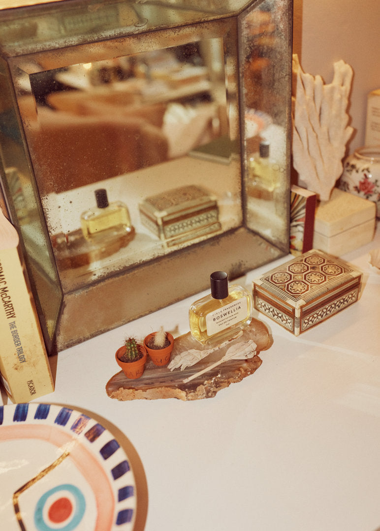 Antique mirror on a white dresser with a perfume bottle, two small cacti on a natural slab, and a patterned wooden box