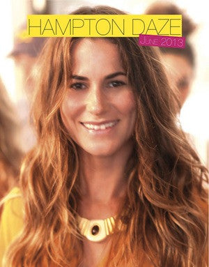 Close-up of a smiling young woman with long wavy light brown hair wearing a yellow top and a gold necklace with a circular pendant