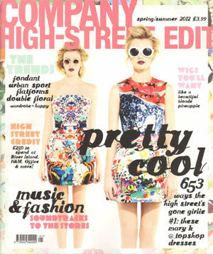 Two young women wearing vibrant floral and graphic patterned dresses with white round sunglasses against a bright studio background