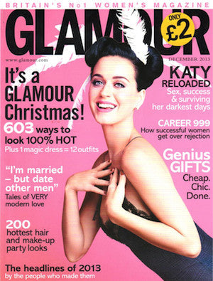 Magazine cover featuring a smiling woman in a black sleeveless dress with white feather hair accessory against a pink background