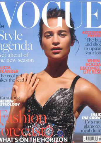 Woman in a shiny black sleeveless dress with thin straps posing against a bright blue sky on a Vogue magazine cover