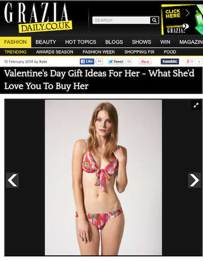 Woman in red and pink floral bikini standing against plain grey background, facing forward with hand near hair