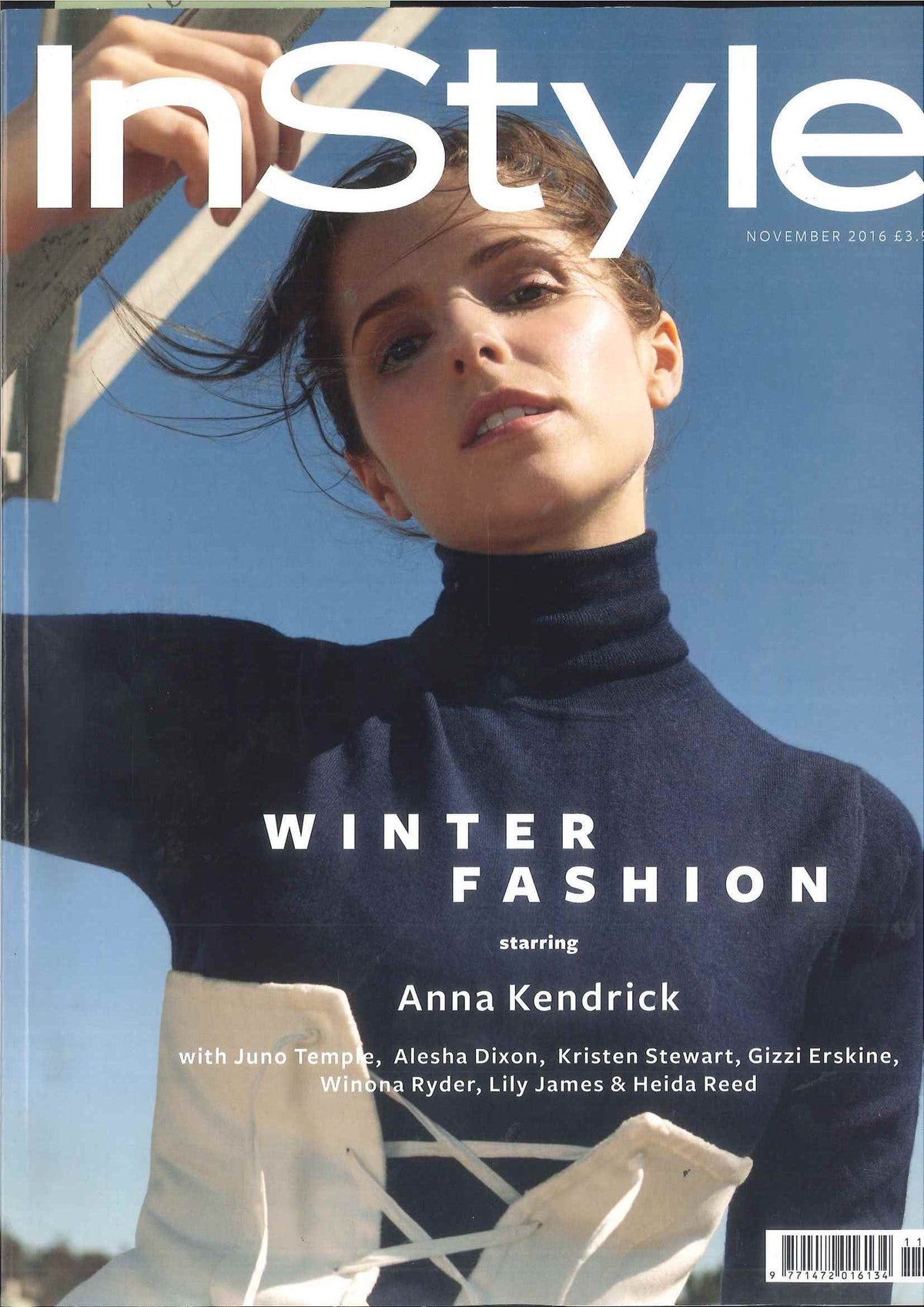 Close-up of a woman in a dark navy turtleneck and white textured gloves against a clear blue sky