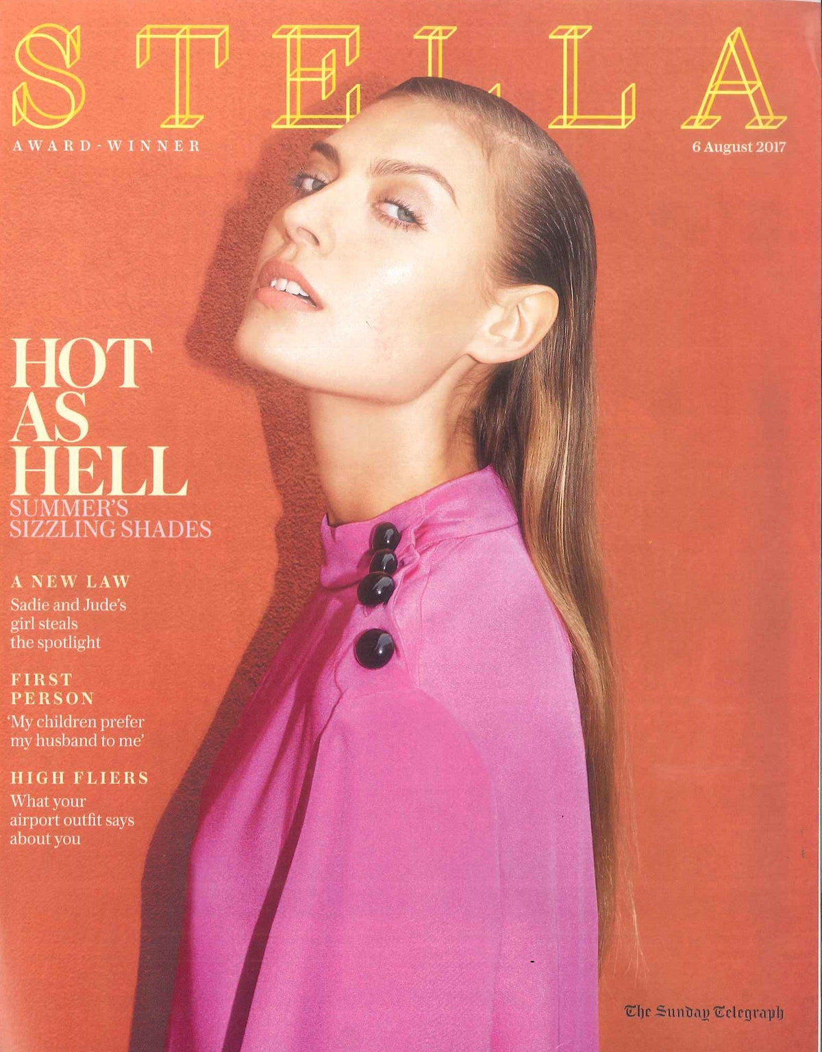 Woman in a bright pink high-neck top with black buttons on the shoulder against an orange-red background, shown in close-up side profile