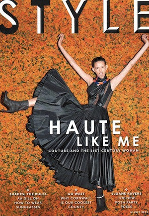 Woman in a black pleated dress with cut-out details and ankle boots posing dynamically against an orange and green textured backdrop
