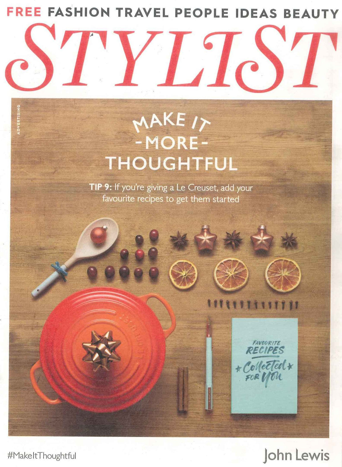 Top-down view of an orange Le Creuset pot with a gold bow, surrounded by spices, dried oranges, and a blue recipe booklet on wood