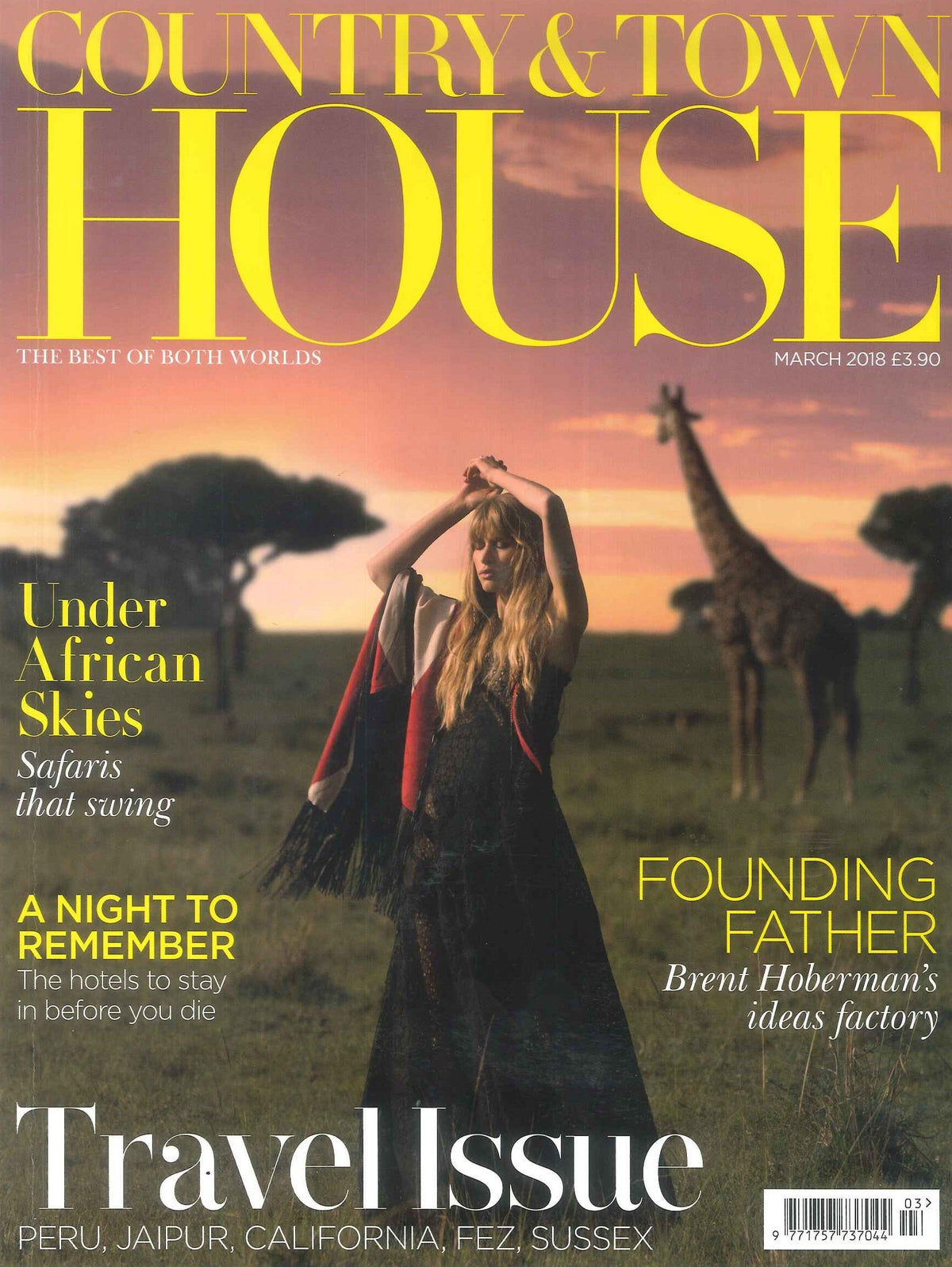 Woman in a black flowing dress holding a red and white fringed shawl on a grassy plain at sunset with a giraffe in the background