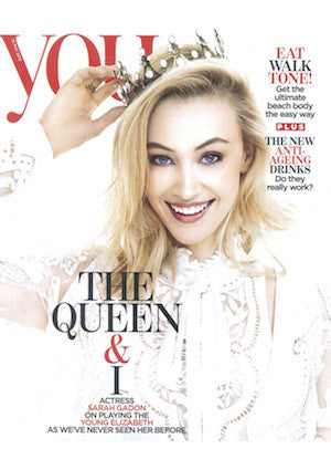 Woman with long blonde hair smiling, wearing white lace top and holding a crown above her head against white background