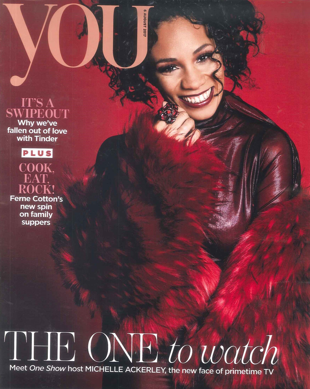 Woman smiling in a shiny dark red leather top and large red and black fur coat, wearing a large flower-shaped ring