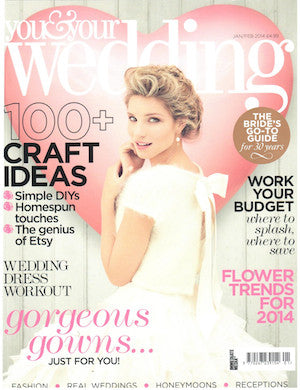 Woman in a white textured wedding gown with short sleeves posing against a pink backdrop shaped like a heart on a bridal magazine cover
