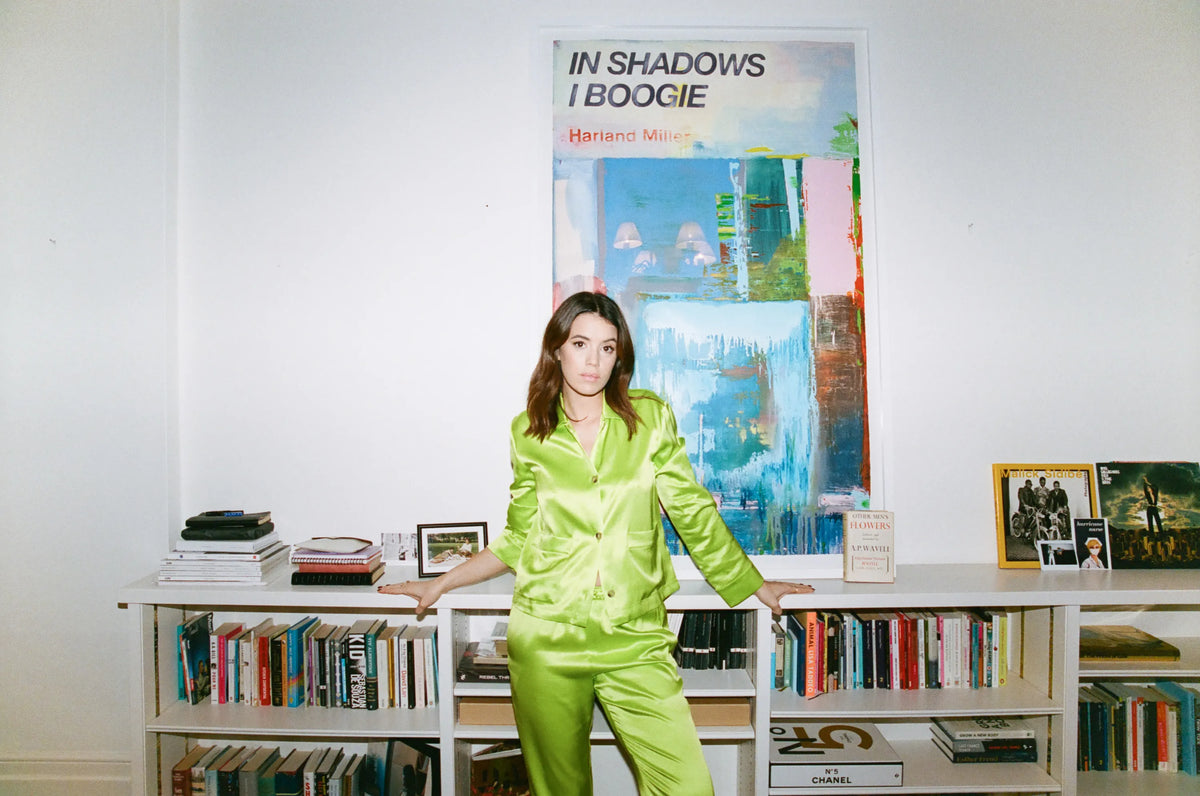 Bright lime green satin pyjama set with buttoned jacket and matching trousers worn by model against a white wall and bookshelf
