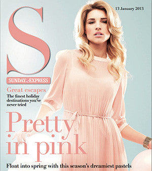 Woman wearing a sheer, long-sleeve, knee-length pink dress with subtle pleats, against a light grey background