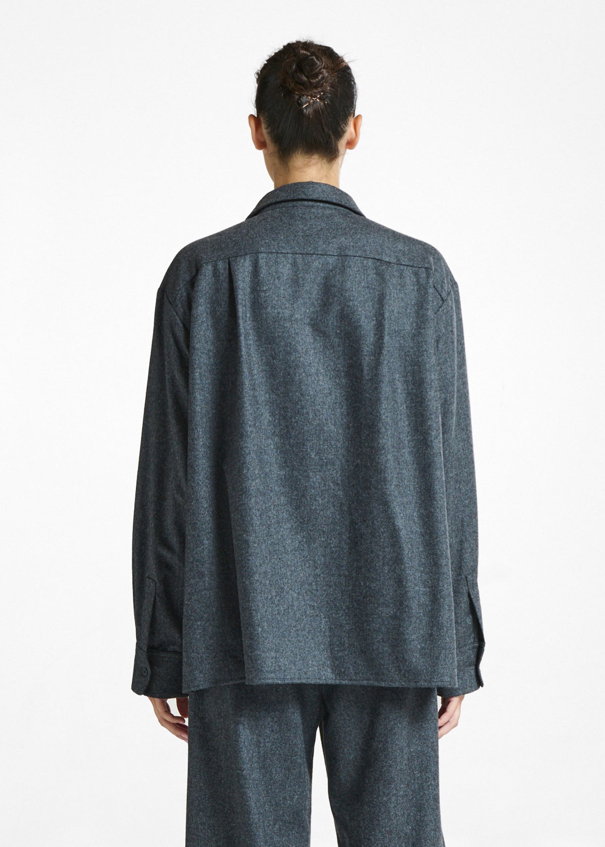 Back view of a model wearing a loose-fitting dark grey wool jacket and matching trousers against a white studio background