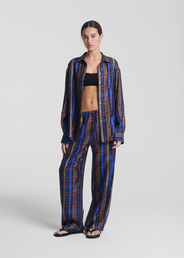 Relaxed-fit blue and brown plaid silk pyjama set with wide-leg trousers and open shirt over a black crop top, styled with black sandals
