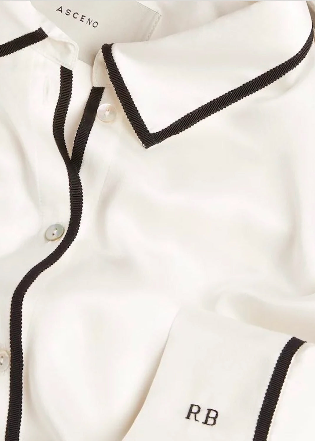 White silk shirt with black trim along collar, button placket, and cuff embroidered with initials 'R.B' in close-up view