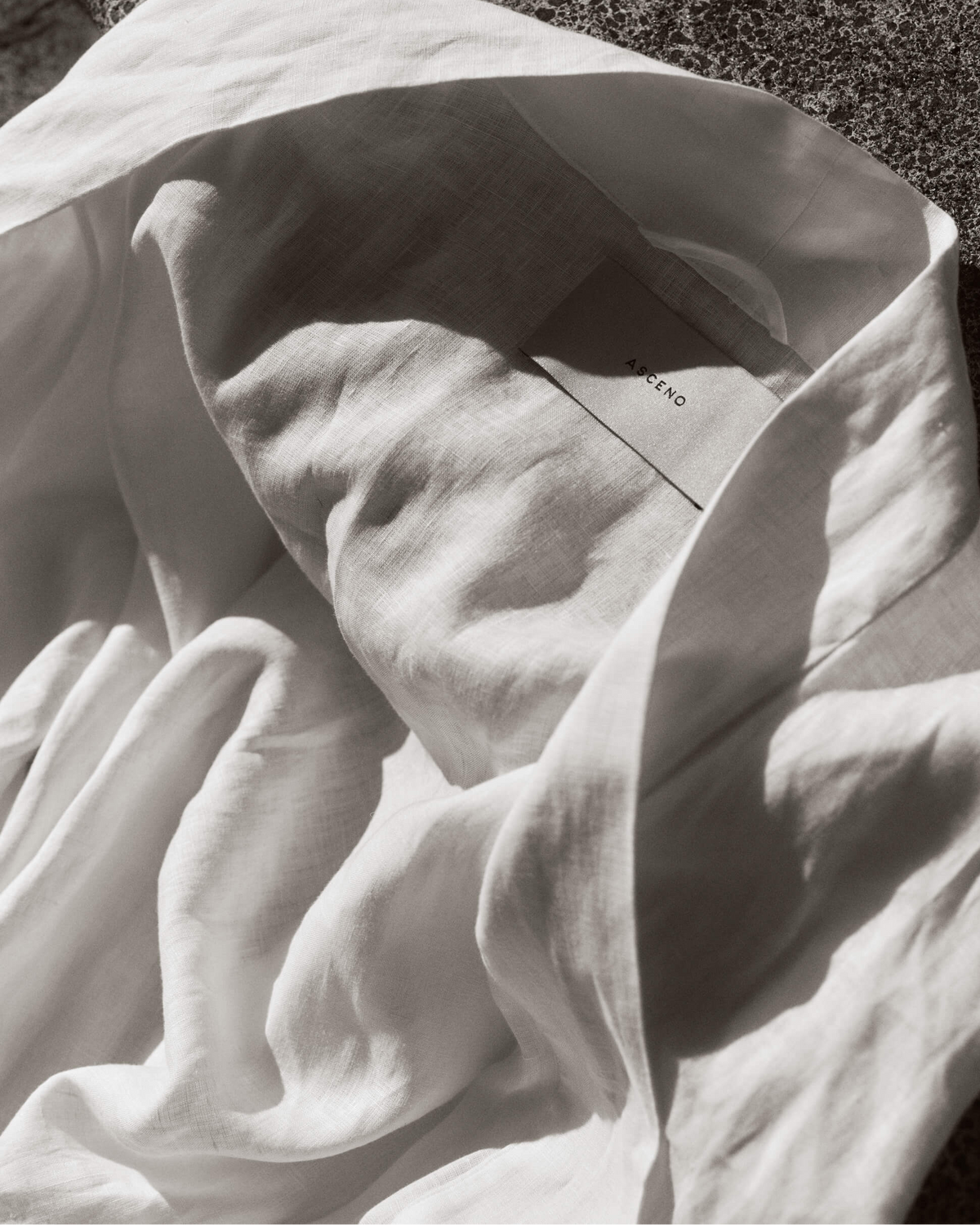 Crumpled white linen fabric with an Asceno label, lit softly to highlight its texture and folds