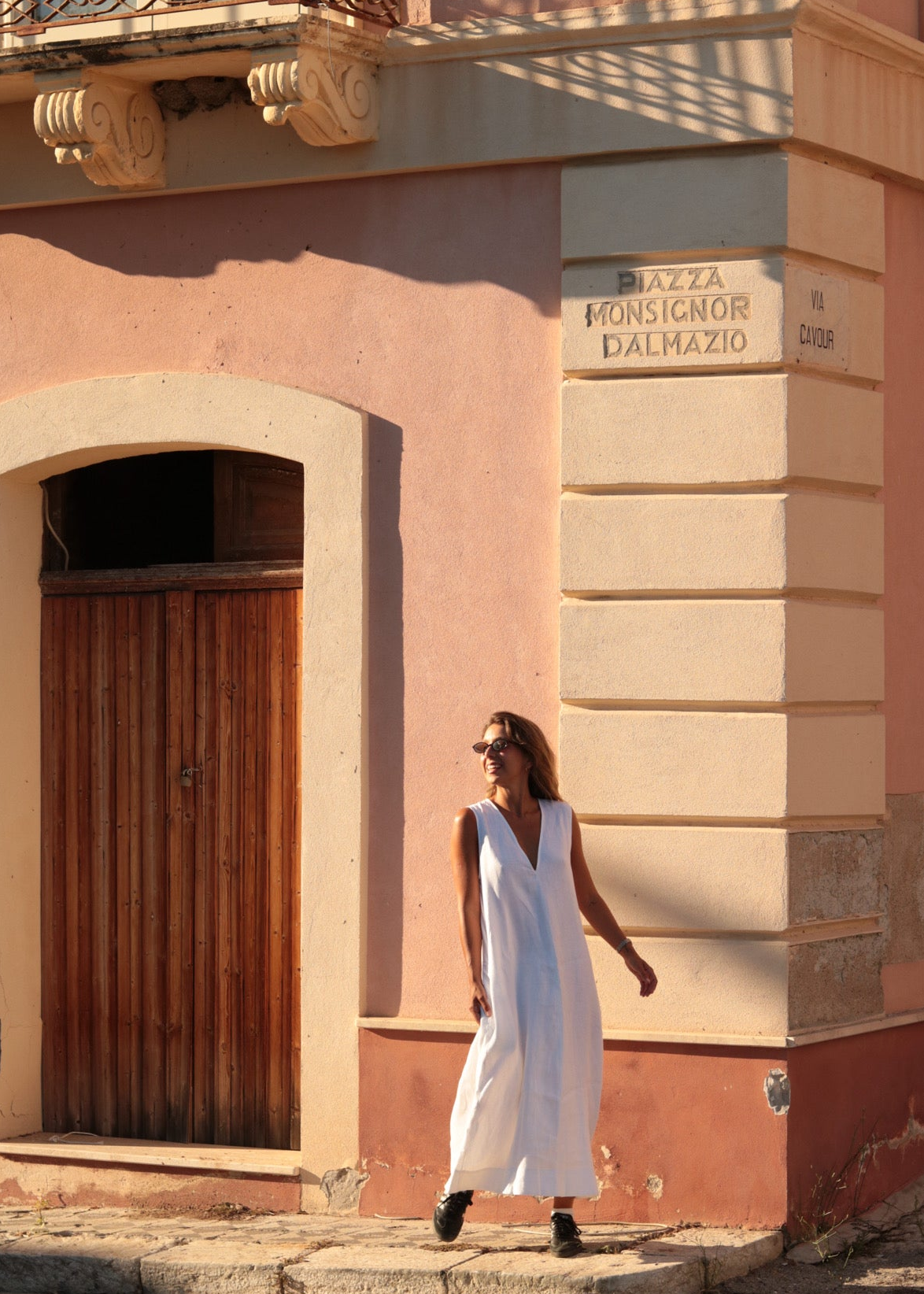 Woman in a white dress walking past a pink building with architectural details.